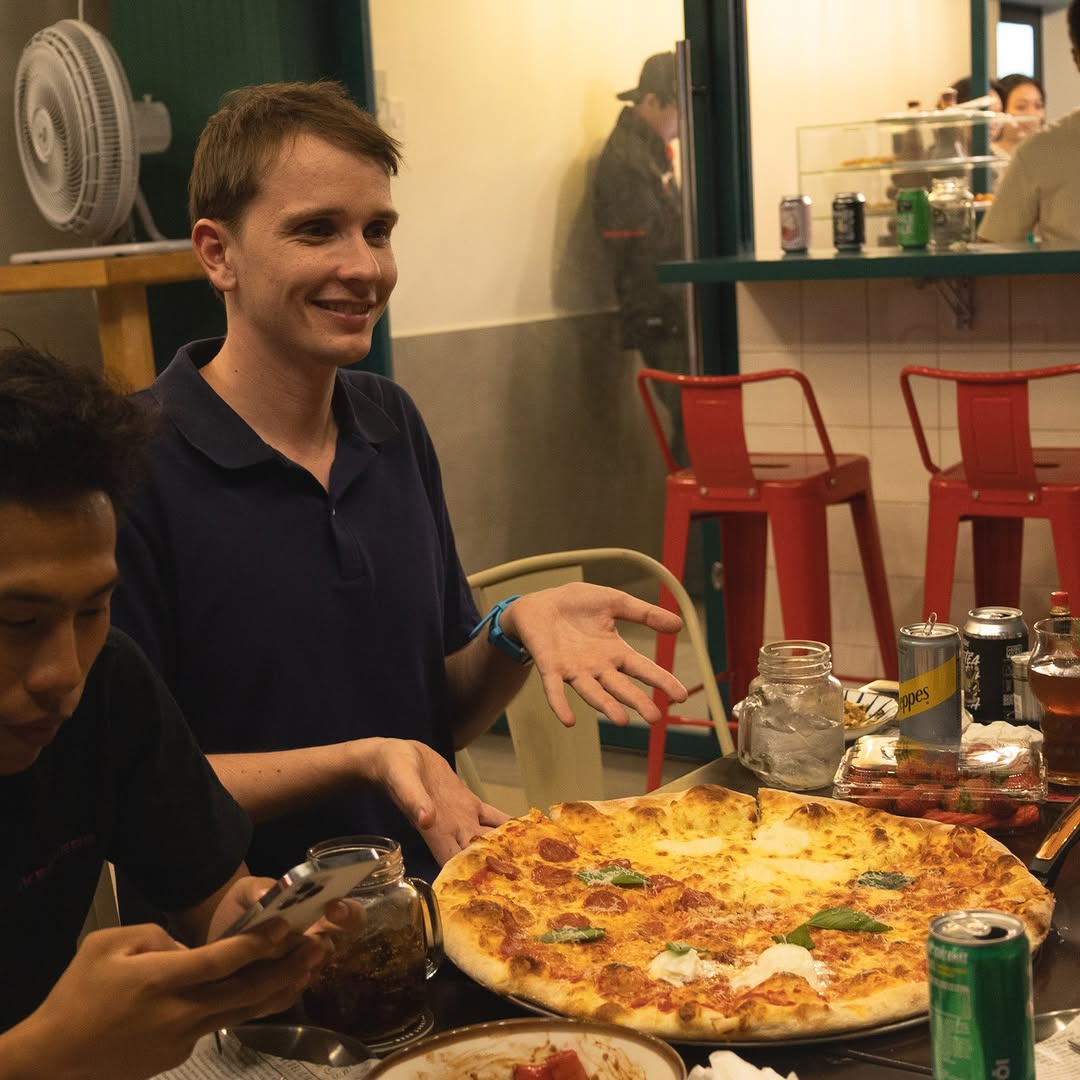 Friends gathered around a custom East Borough pizza pie with drinks at the table.