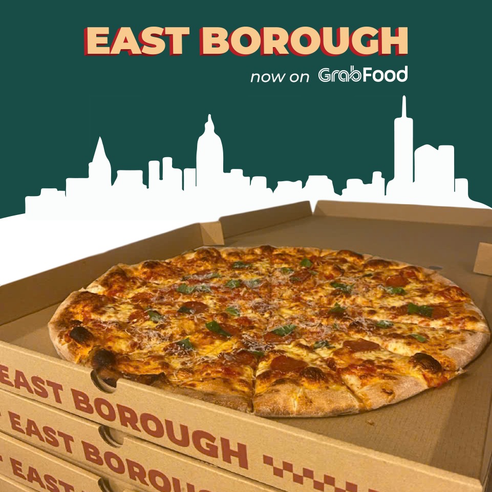 A whole pizza on a stack of East Borough branded boxes, with a New York skyline graphic behind.