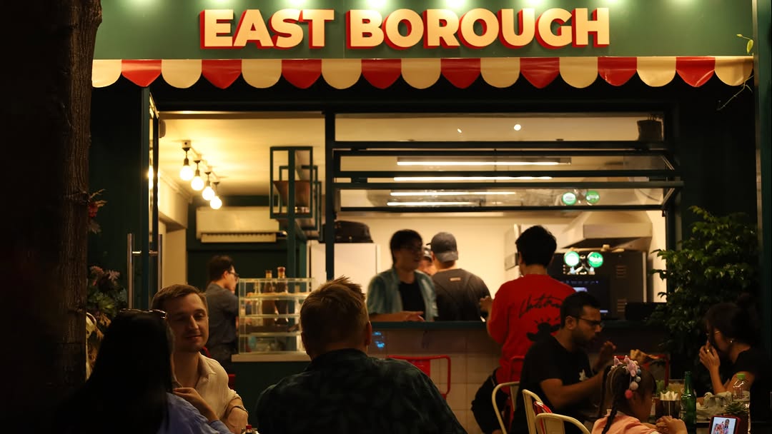 The East Borough shopfront at night — red and cream scalloped awning under a lit sign, kitchen open behind the counter.